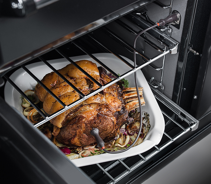 Oven door is open revealing a joint of meat with a meat probe in it.